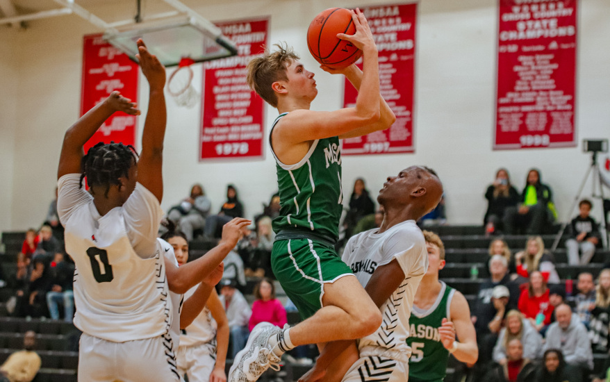 boy shooting basketball and other boys blocking