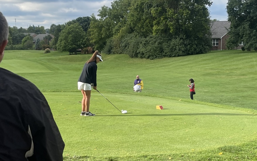 girl hitting golf ball as people watch